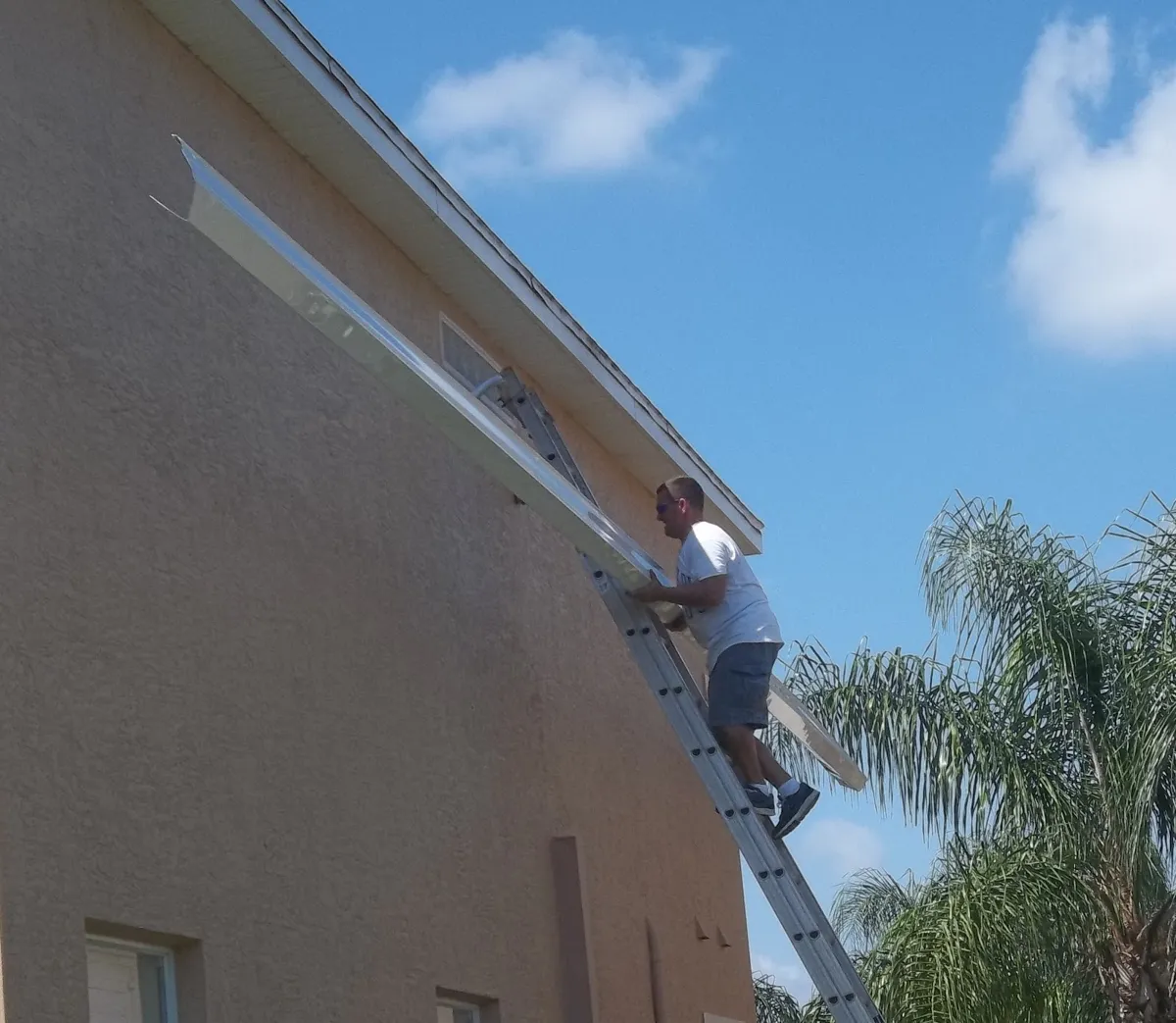 Installer on an extension ladder fitting a long gutter run on a two-story stucco house